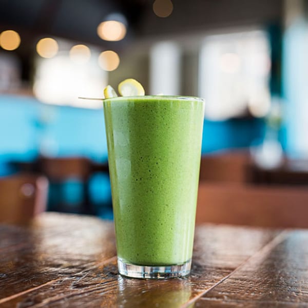 A tall glass of green smoothie with lemon slices on a wooden table at Beerline Cafe.