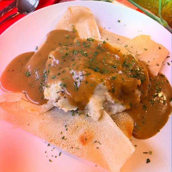 Savory crepes filled with mashed potatoes and covered in brown gravy and parsley.