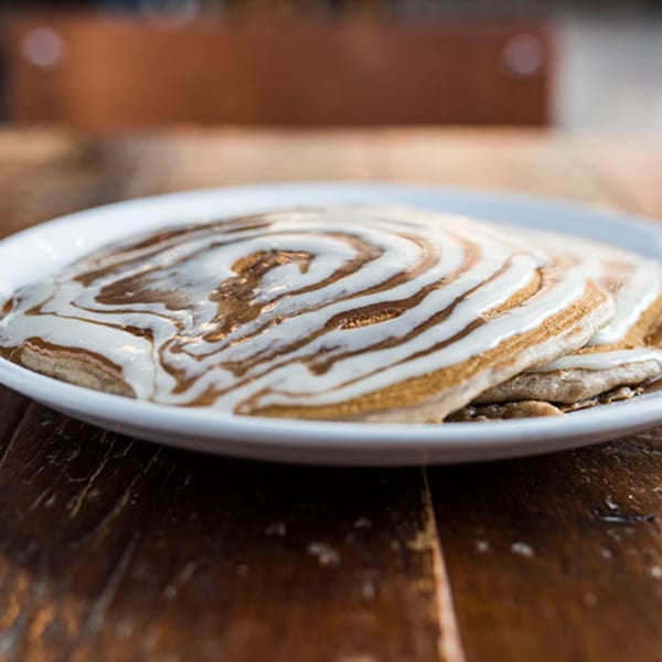 A stack of pancakes with white and brown swirled icing on a white plate.