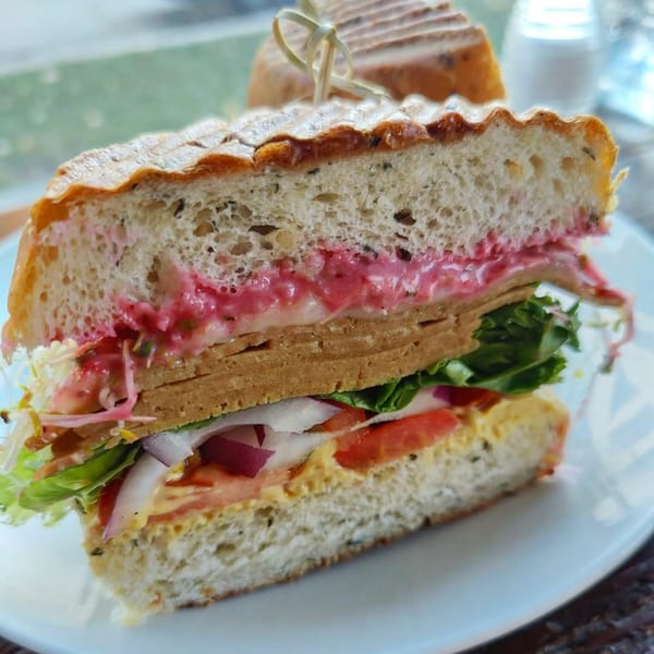 A grilled vegetarian panini from Beerline Cafe, filled with pink sauce, plant-based protein, lettuce, and tomato.