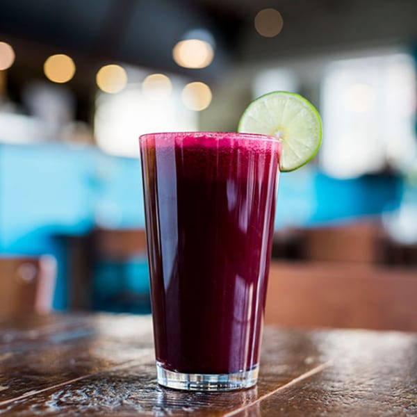 A tall glass of vibrant red beet juice with a lime slice on a wooden table.