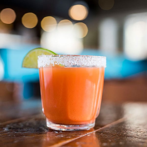 Orange cocktail with a salted rim and lime wedge on a wooden table at Beerline Cafe.