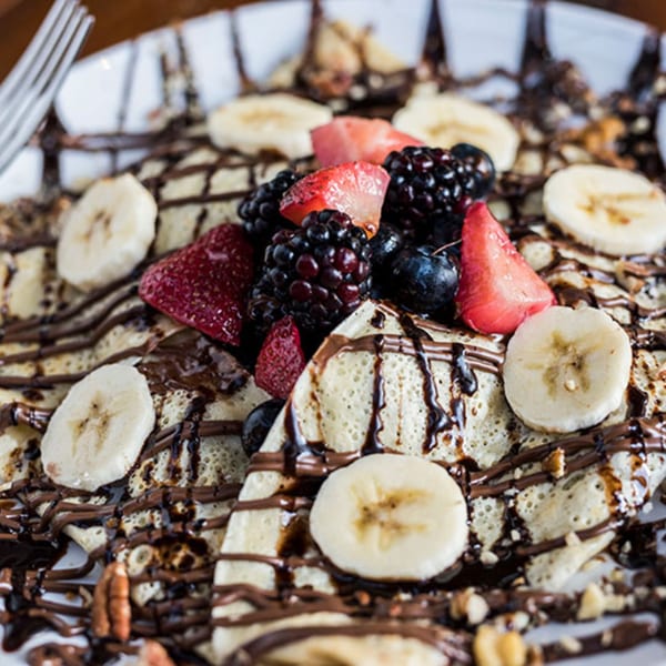 Crepes drizzled with chocolate, topped with fresh strawberries, blueberries, blackberries, and banana slices.