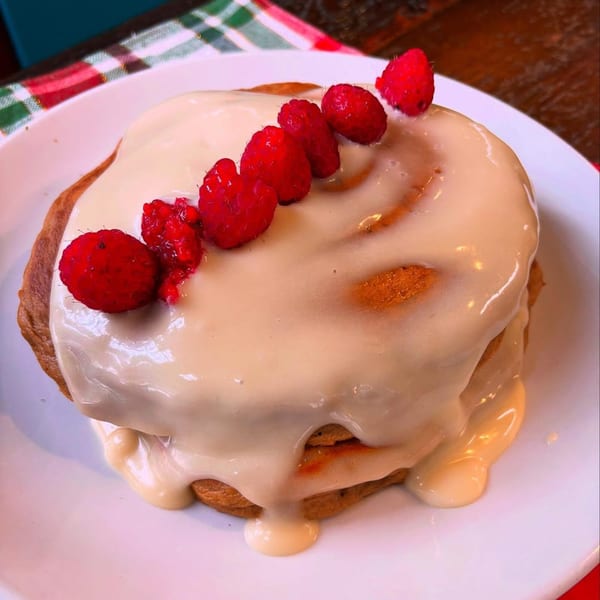 Vegan cinnamon roll with white icing and a line of fresh raspberries on a white plate.