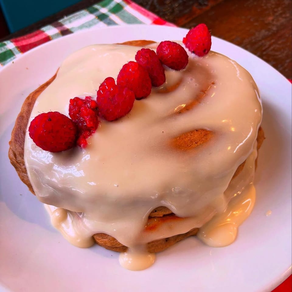 Vegan cinnamon roll with white icing and a line of fresh raspberries on a white plate.
