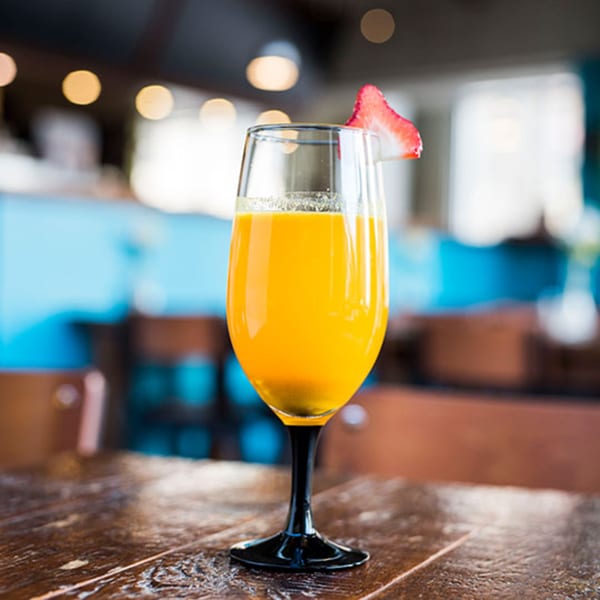 A mimosa cocktail with a strawberry garnish sits on a wooden table at Beerline Cafe.