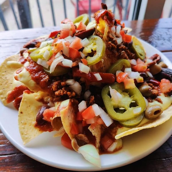 Vegetarian nachos piled high with cheese, salsa, jalapeños, olives, and diced onions on a white plate.